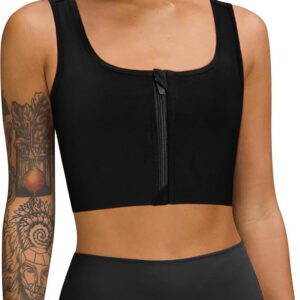 A person wearing a LEINIDINA black ftm chest binder with a front zippered closure and black high-waisted leggings. The individual boasts tattoos on their arms, showcasing intricate designs against the plain white background.