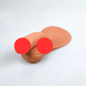 A skin-toned, ivory & beige p*nis with two red circles overlies a shiny, smooth surface. The object appears to have a semi-cylindrical, folded section resting on a flattened part. The background is plain and white.
