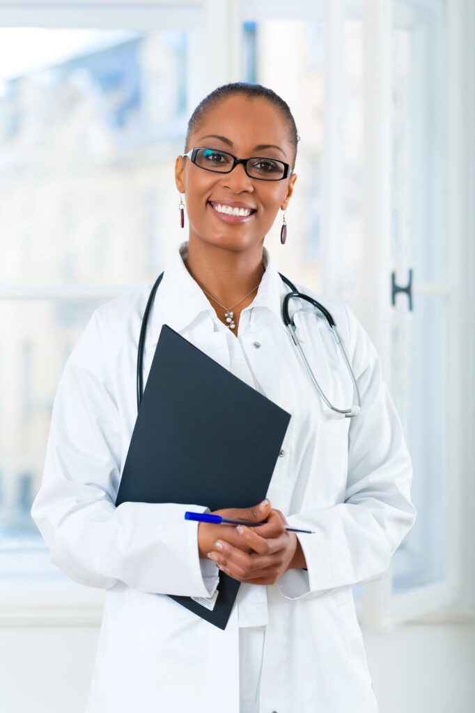 Black female doc A smiling doctor in a white coat and stethoscope holds a black folder and pen, ready to discuss transmasculine HRT.