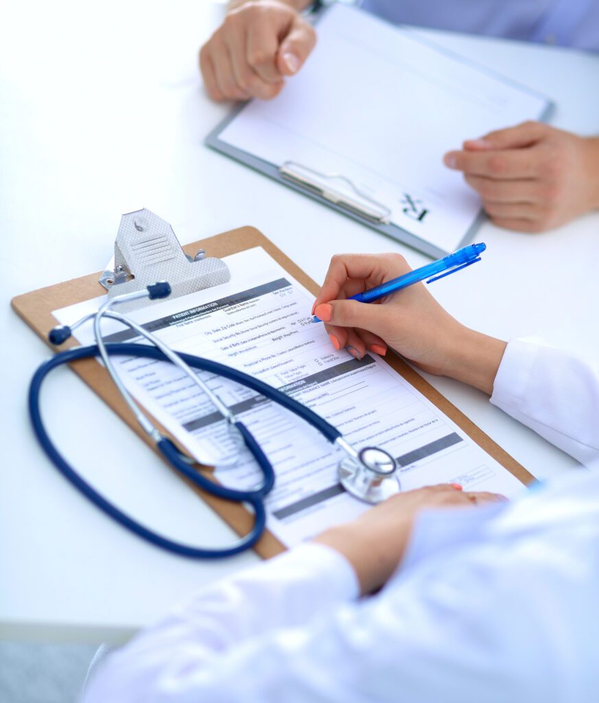 clipboard rx form A doctor fills out a transmasculine patient’s registration form on a clipboard with a stethoscope resting on top, while the patient holds a testosterone prescription pad across the table.