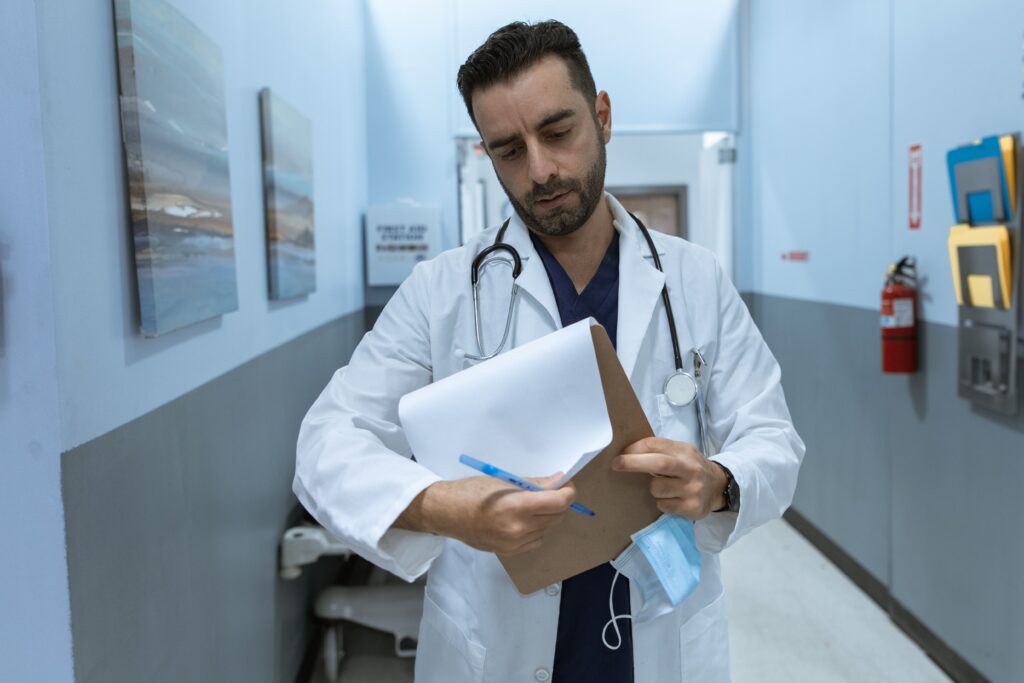 pexels-photo-6129112-6129112 A doctor in a lab coat reviews a medical chart in a hospital hallway.