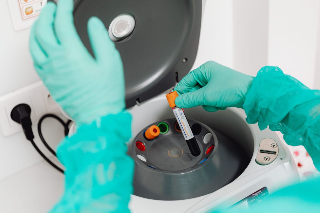 pexels-photo-6627687-6627687 A lab technician wearing gloves uses a centrifuge for blood analysis in a modern laboratory setting.
