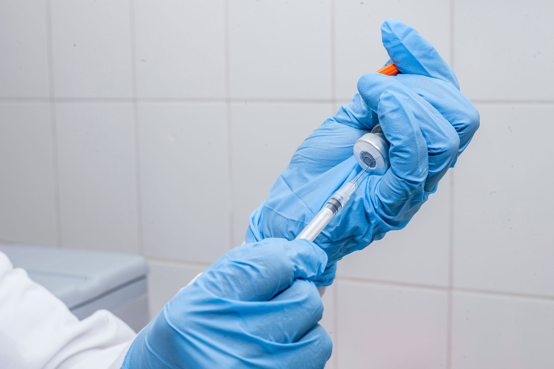 hands in blue gloves transferring a liquid from the bottle using a syringe